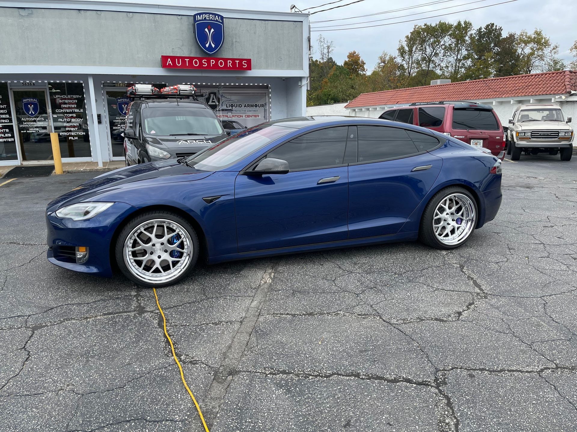 A blue Tesla model s is parked in a parking lot in front of a building.