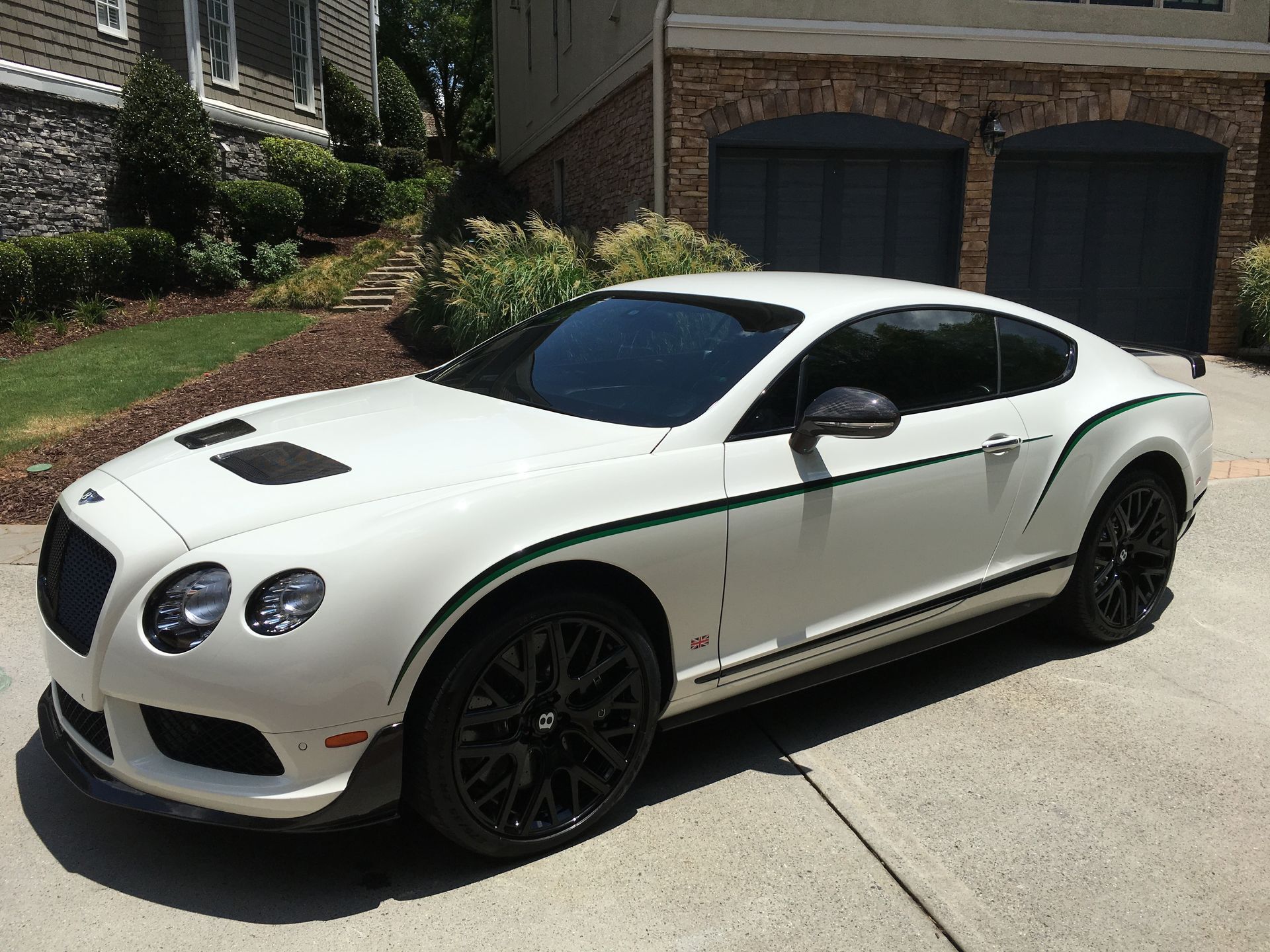 A white Bentley is parked in a driveway in front of a garage.