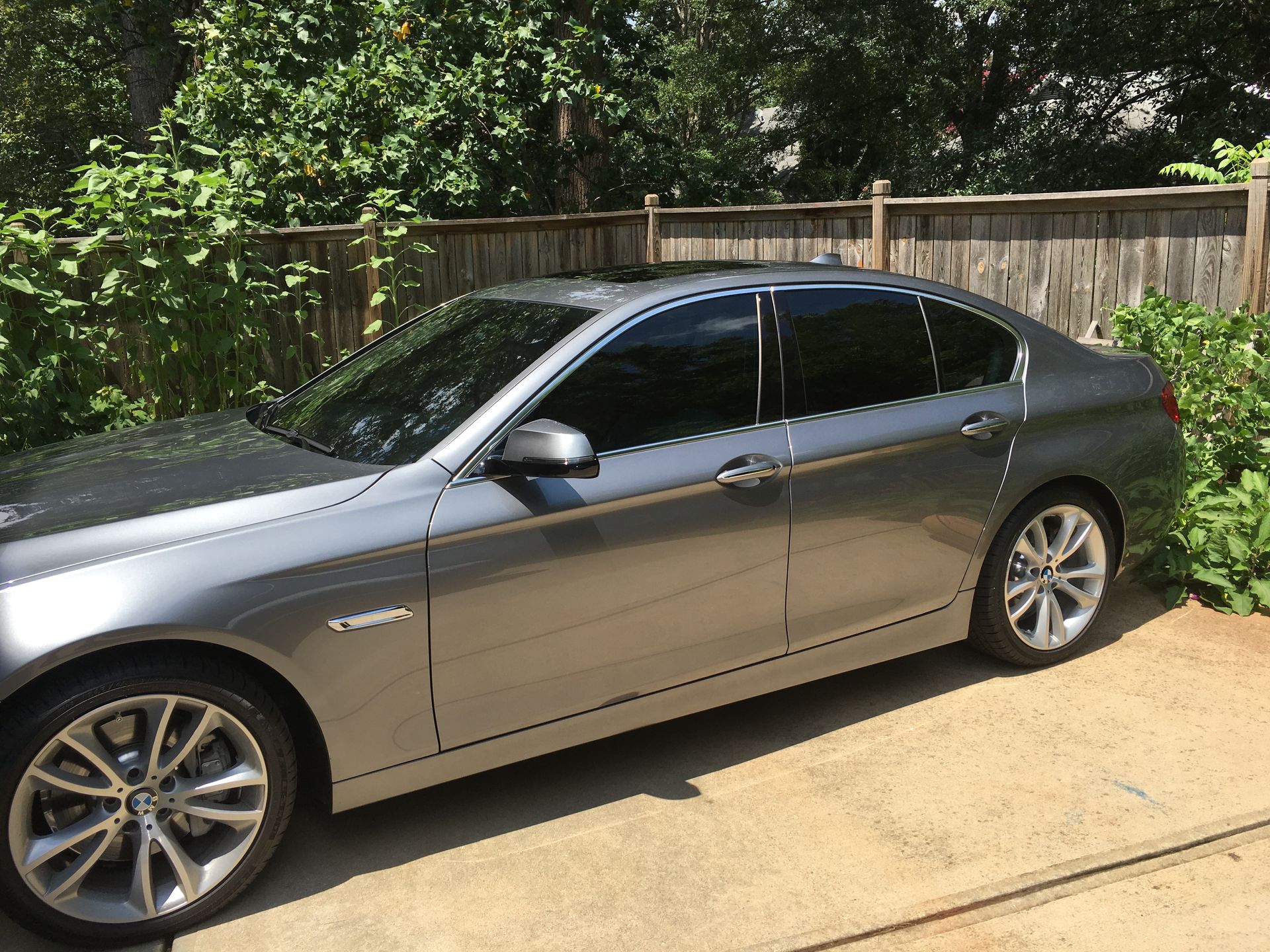 A gray car is parked in a driveway next to a fence.