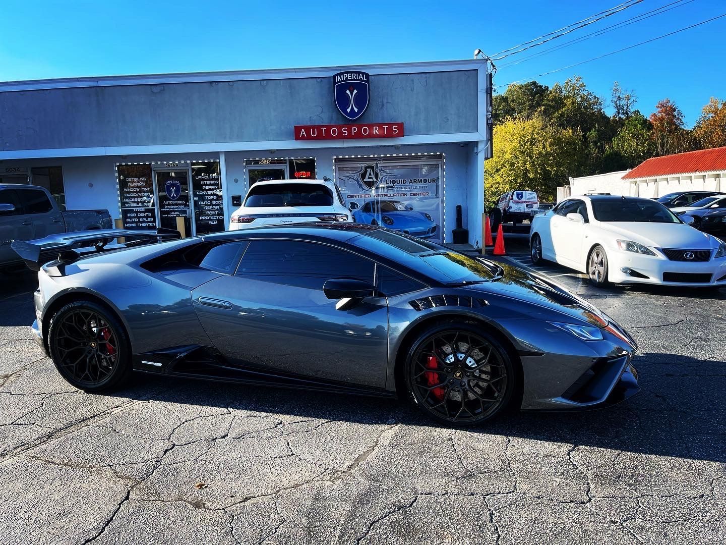A silver Lamborghini Huracan is parked in front of a car dealership.