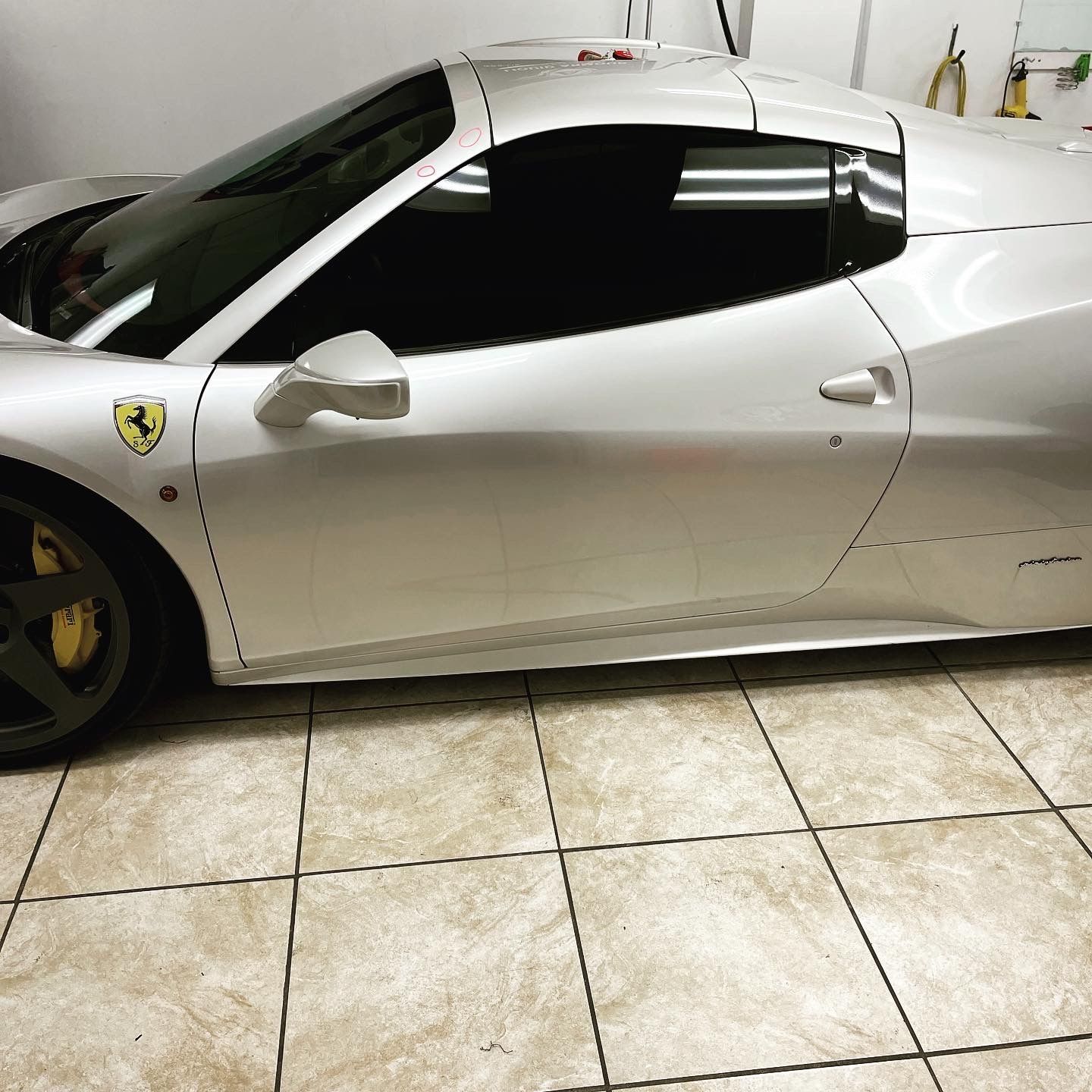 A silver Ferrari is parked on a tiled floor in a garage.