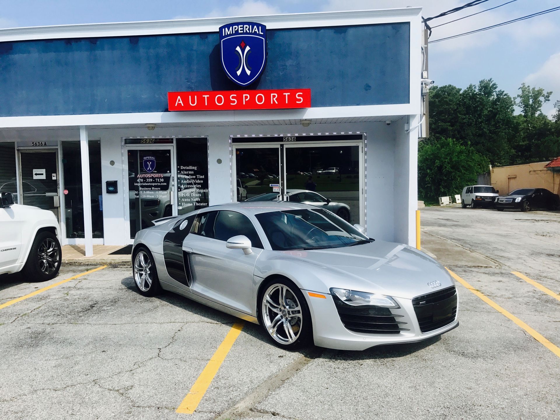 A silver sports car is parked in front of an auto sports store