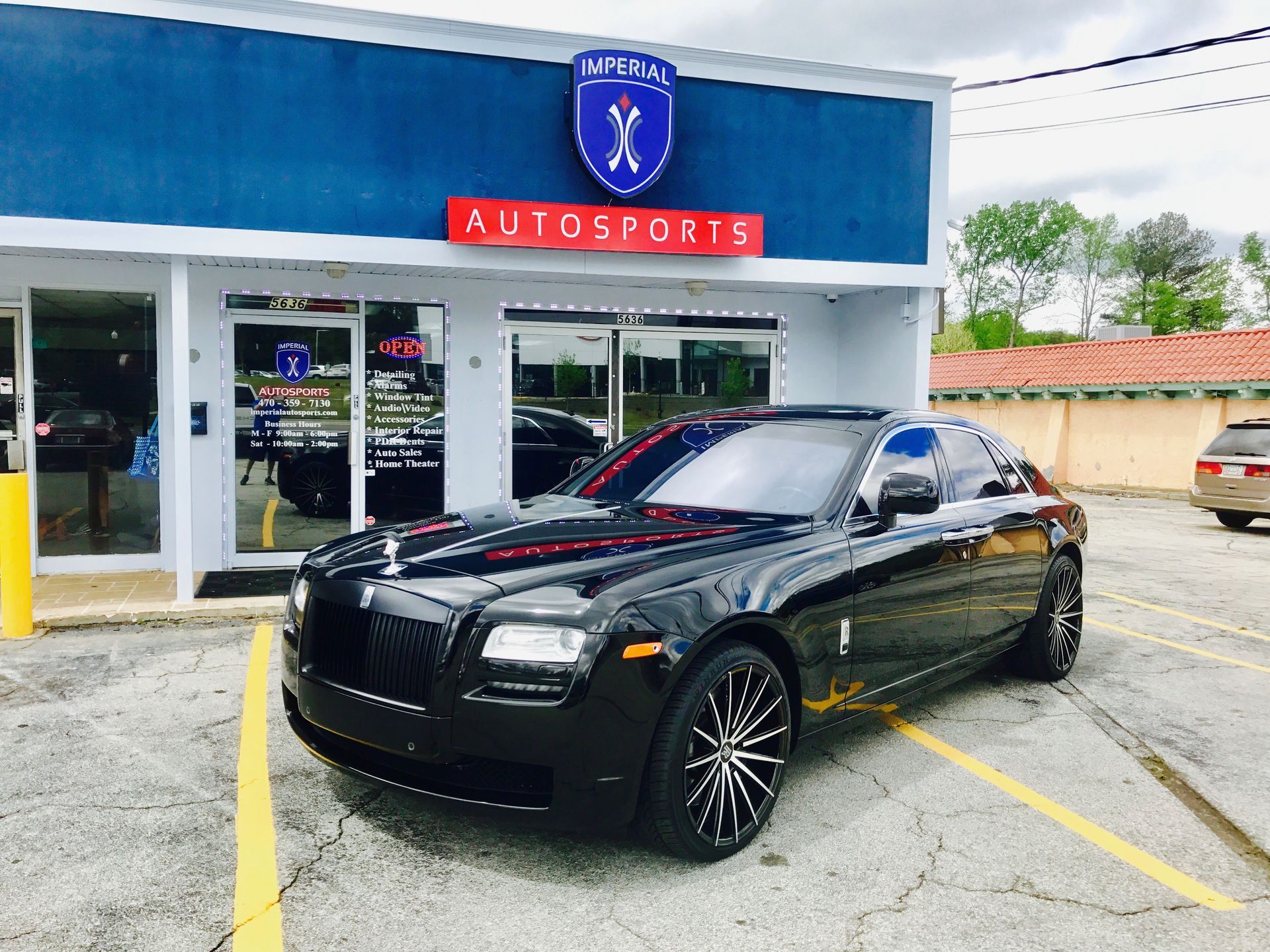A good-looking black car is parked in front of a car dealership.