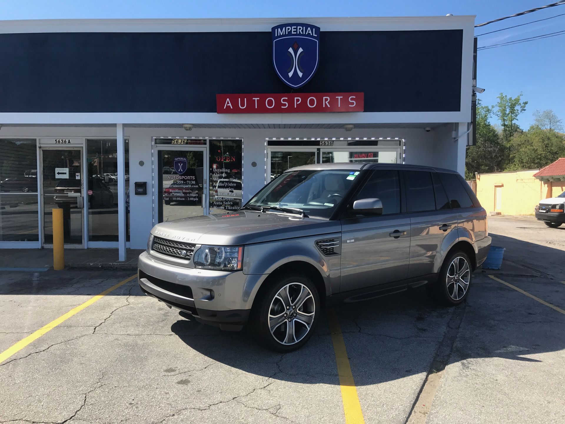 A silver Range Rover is parked in front of a car dealership.