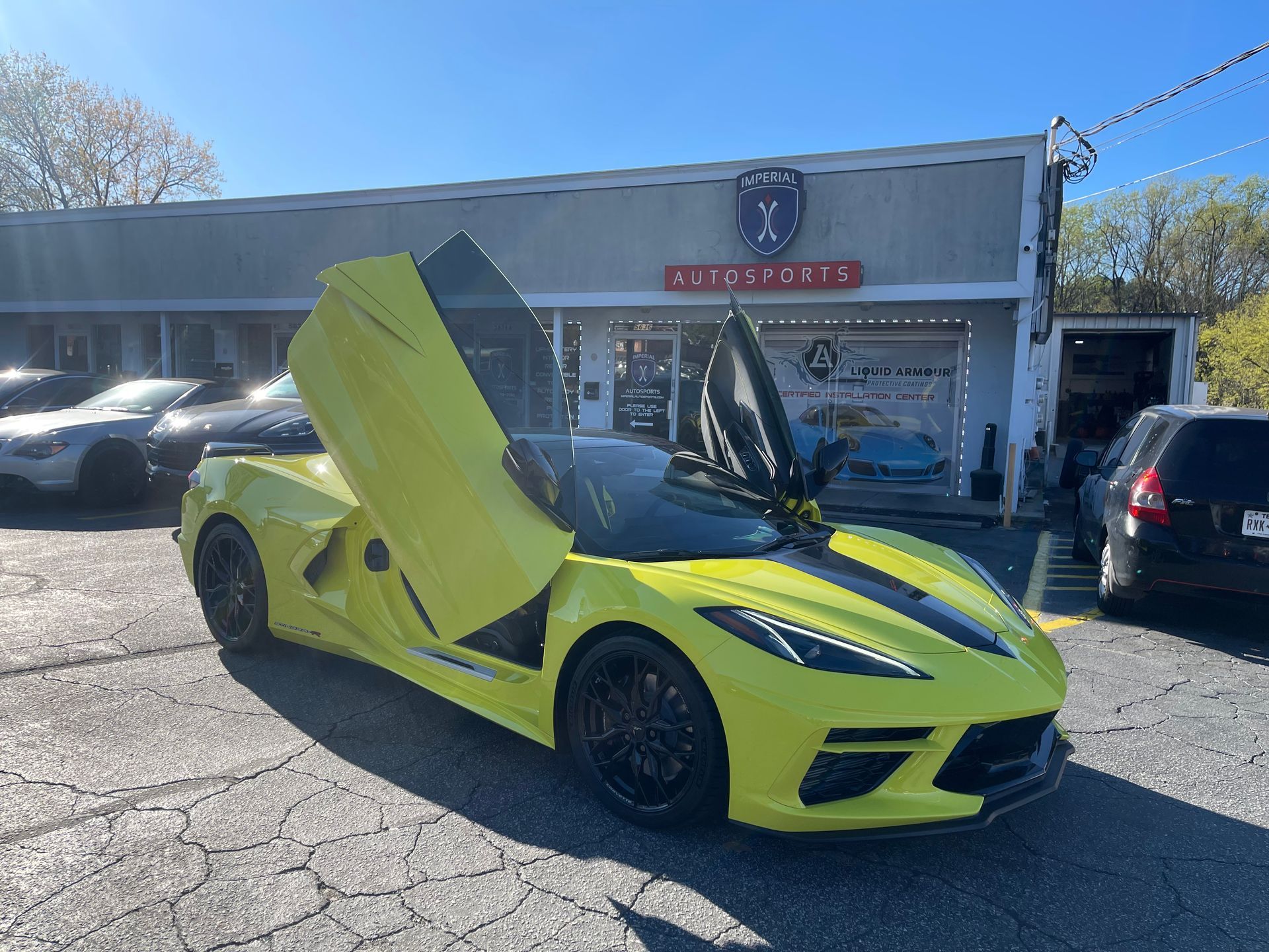 A yellow-green sports car is parked in front of a car dealership.