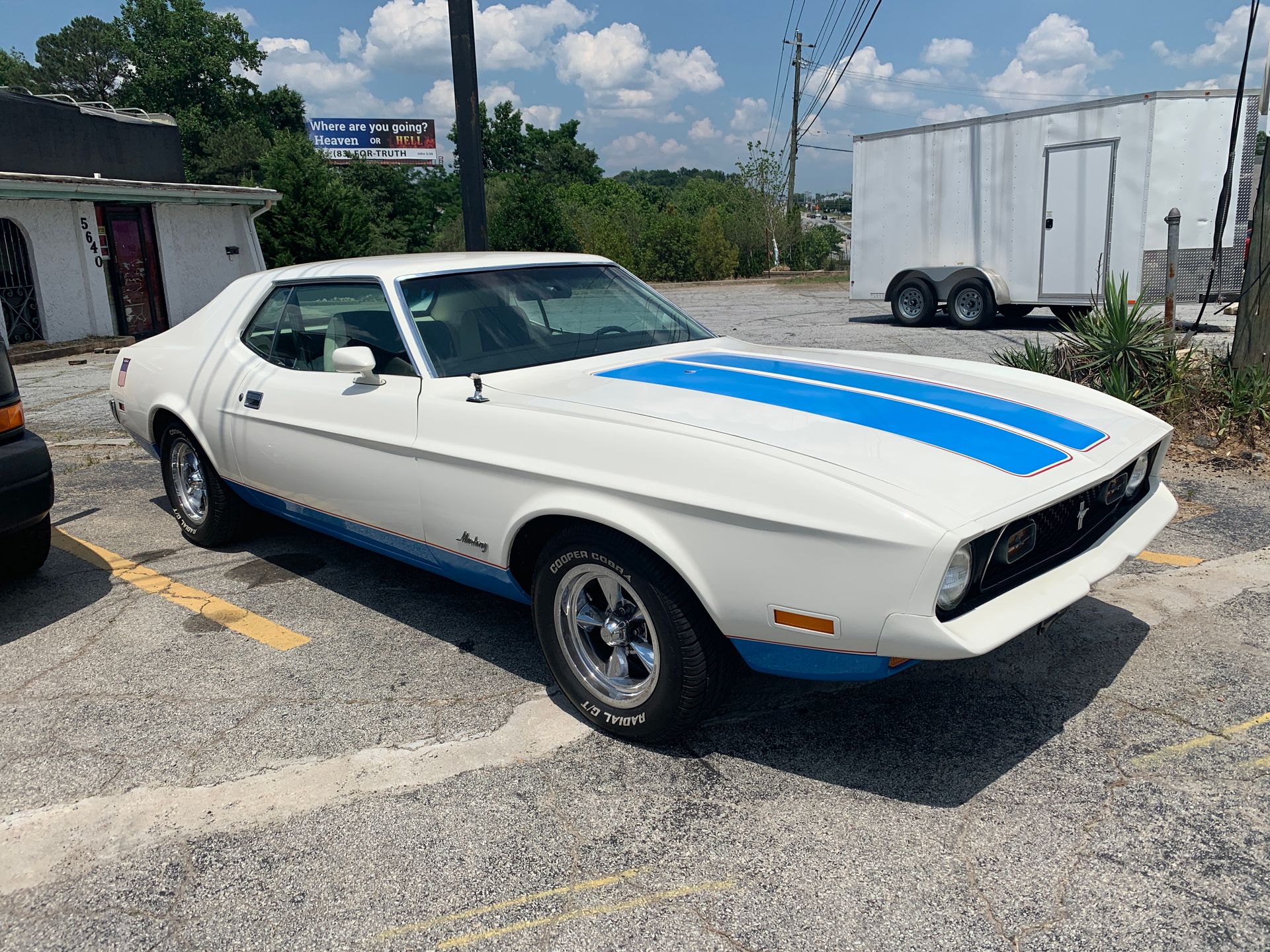 A white Mustang with blue stripes is parked in a parking lot.