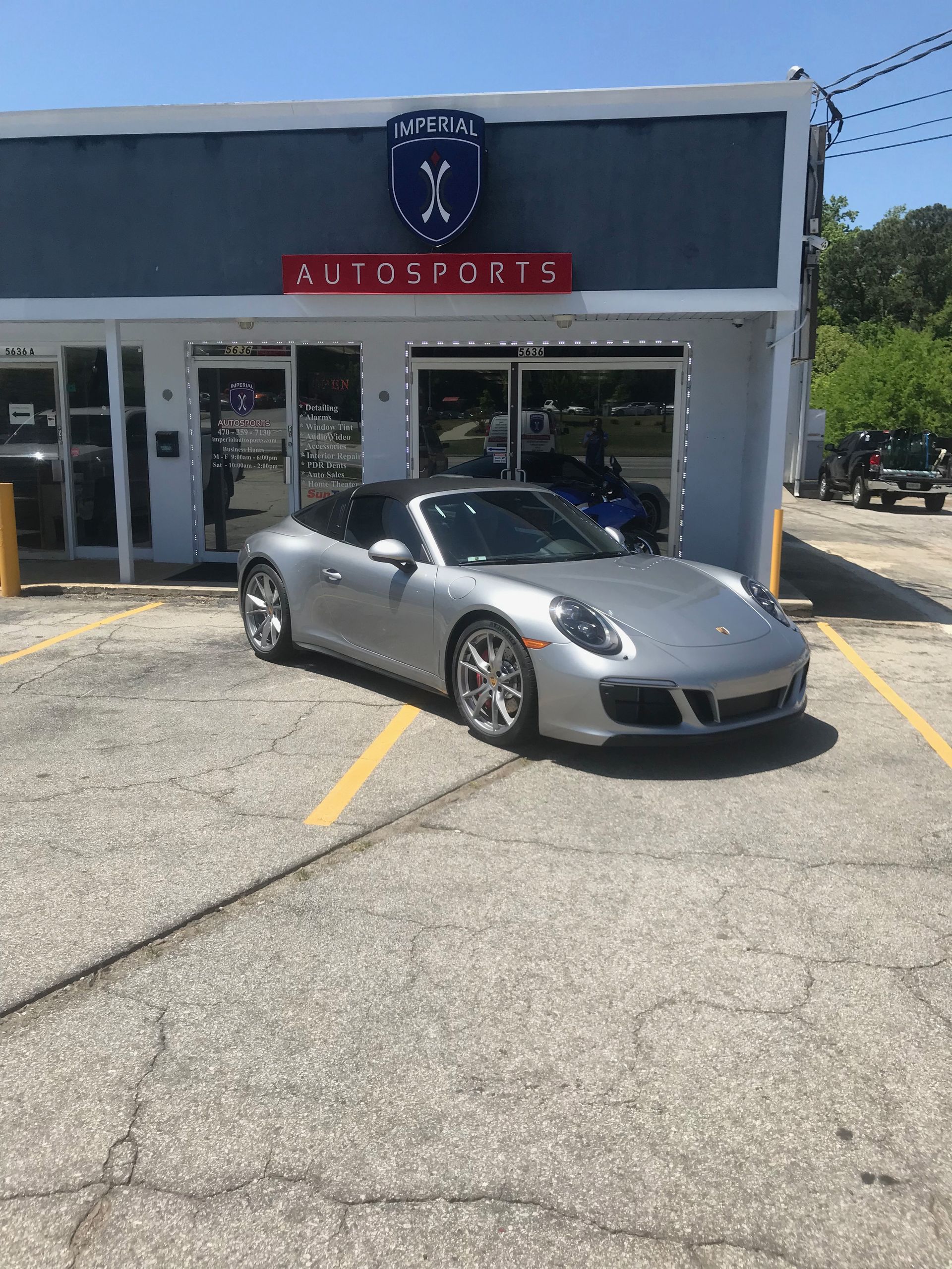 A silver Porsche 911 Carrera GTS is parked in front of a car dealership.