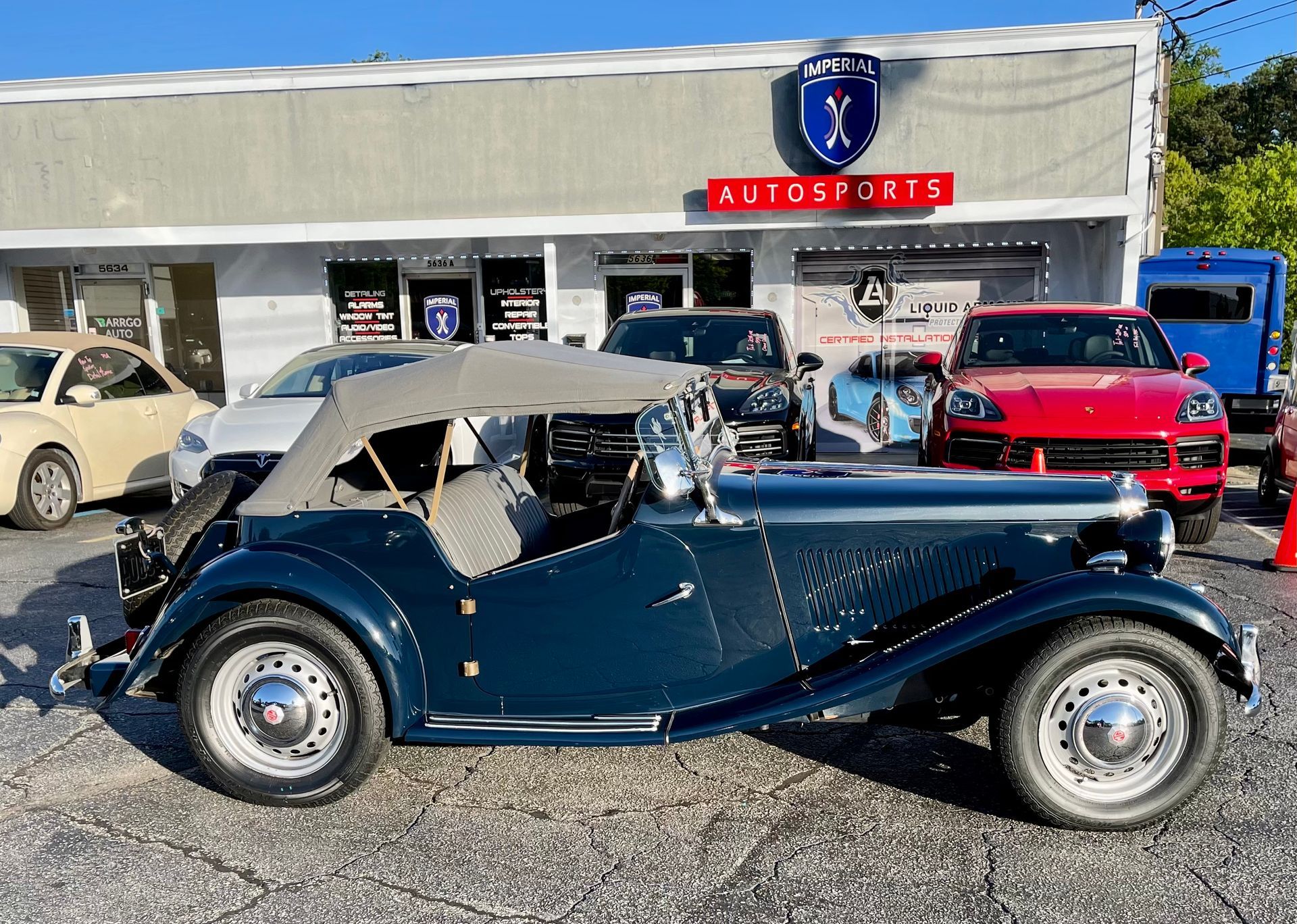 A blue car is parked in front of a car dealership.