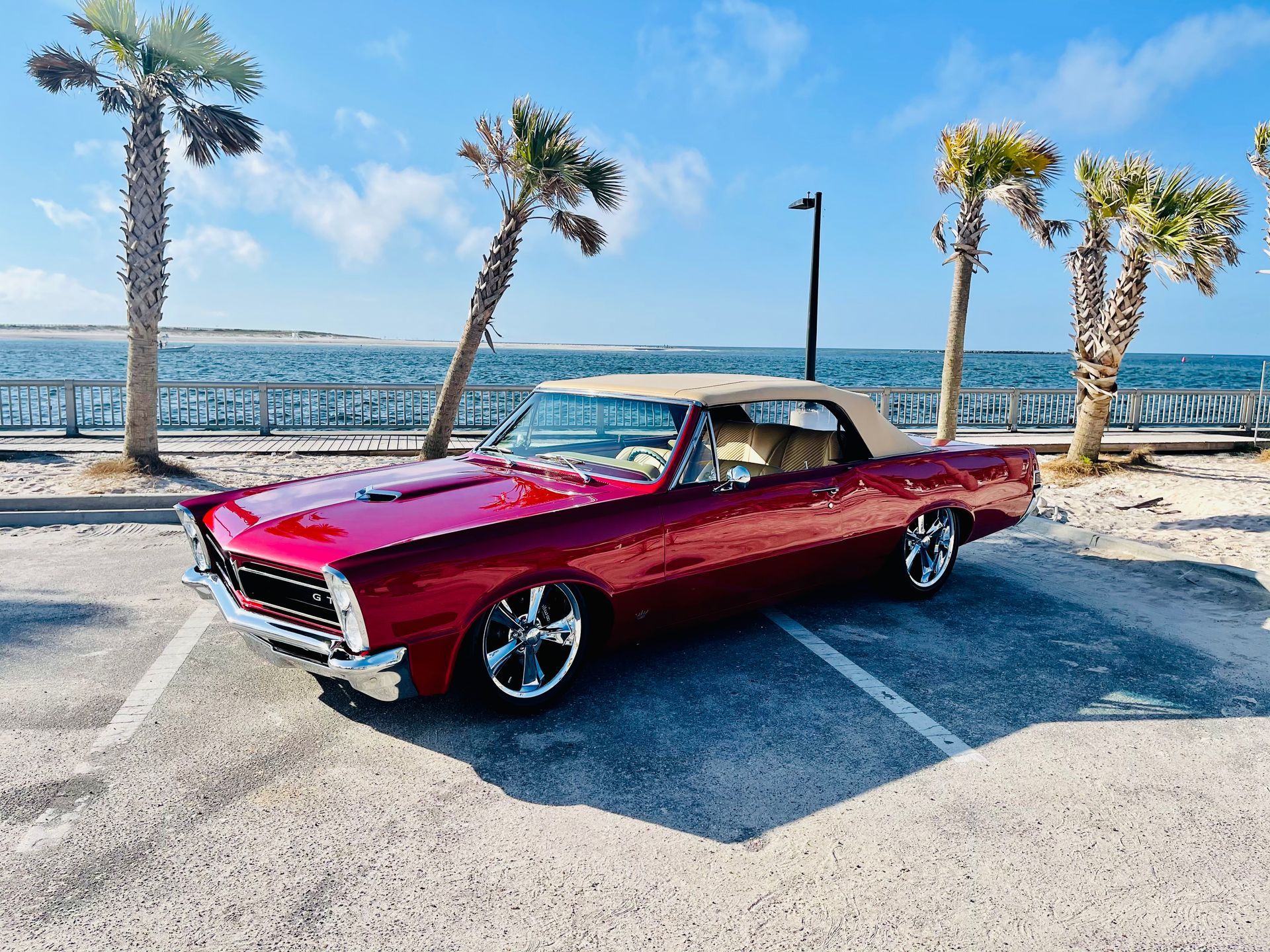 A red convertible car is parked in a parking lot near the ocean.