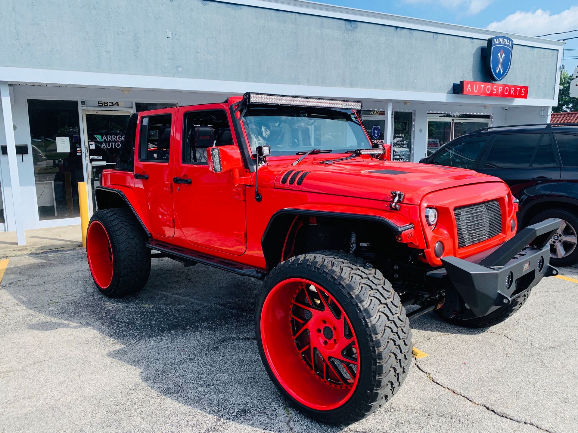 A red Jeep with red wheels is parked in front of a building.