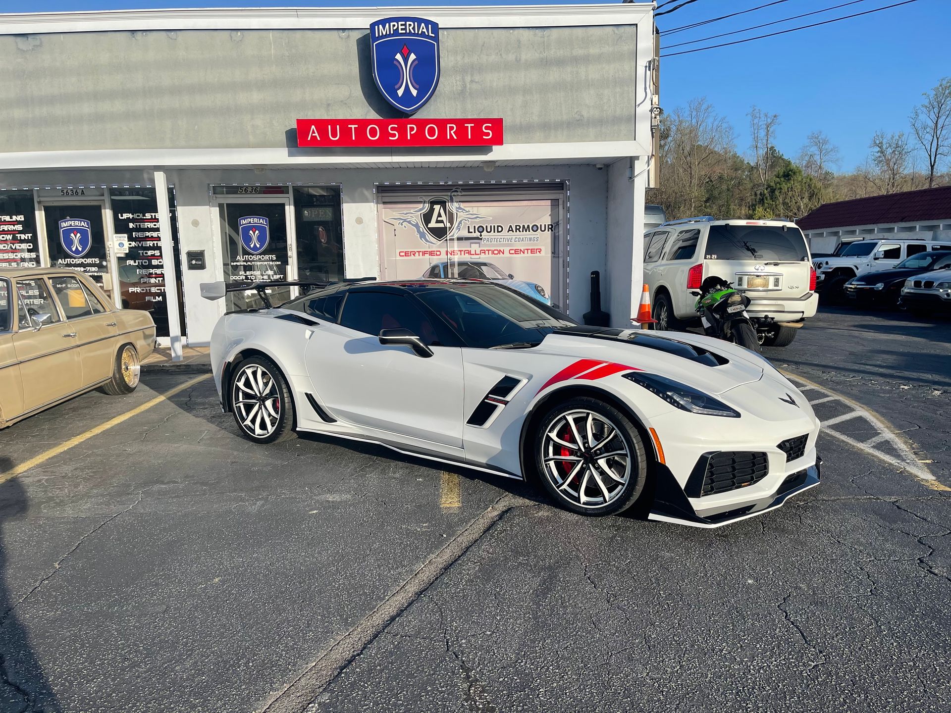 A white Corvette ZR1 is parked in front of a car dealership.