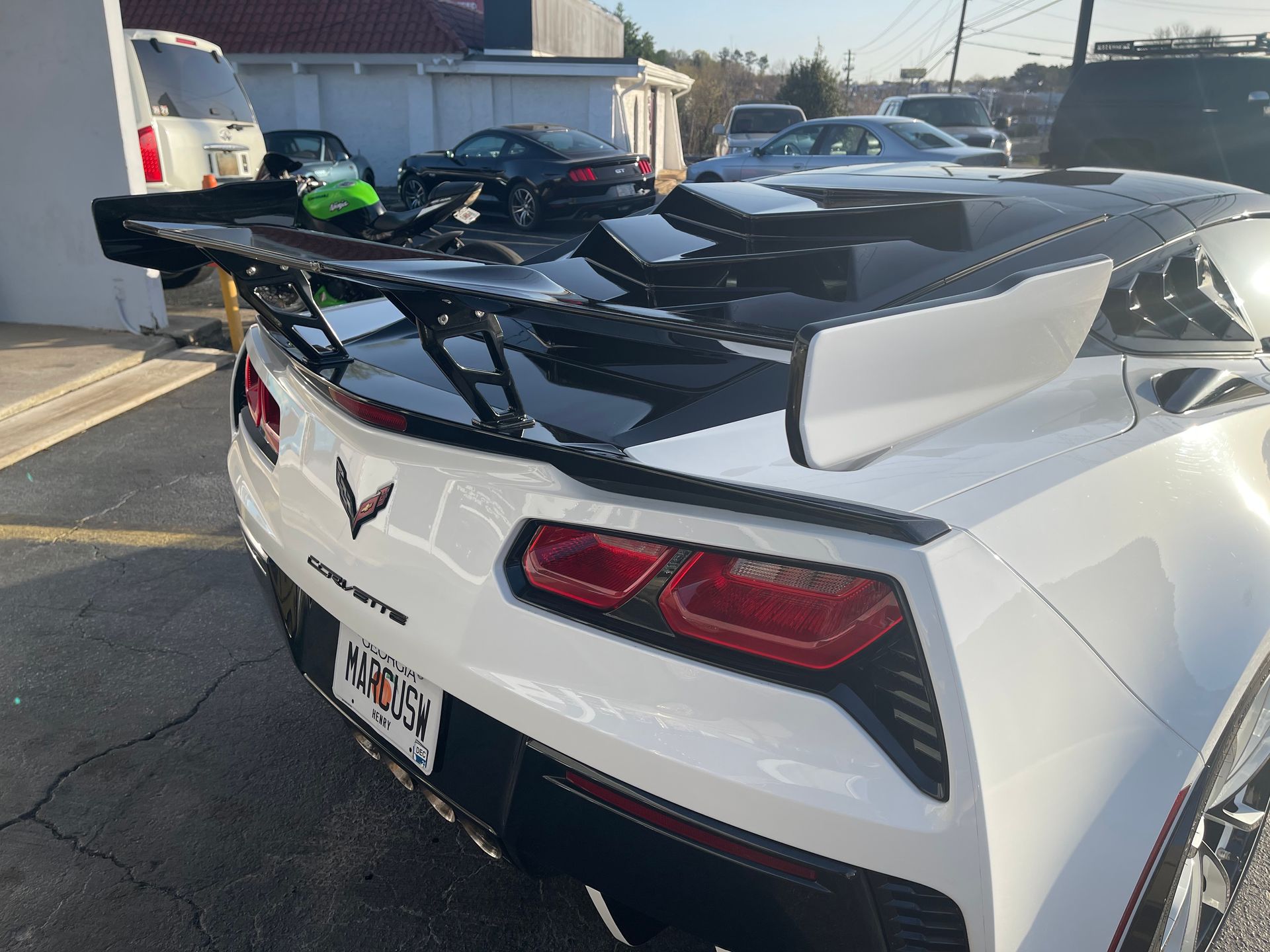 A white Corvette with a black spoiler is parked in a parking lot.