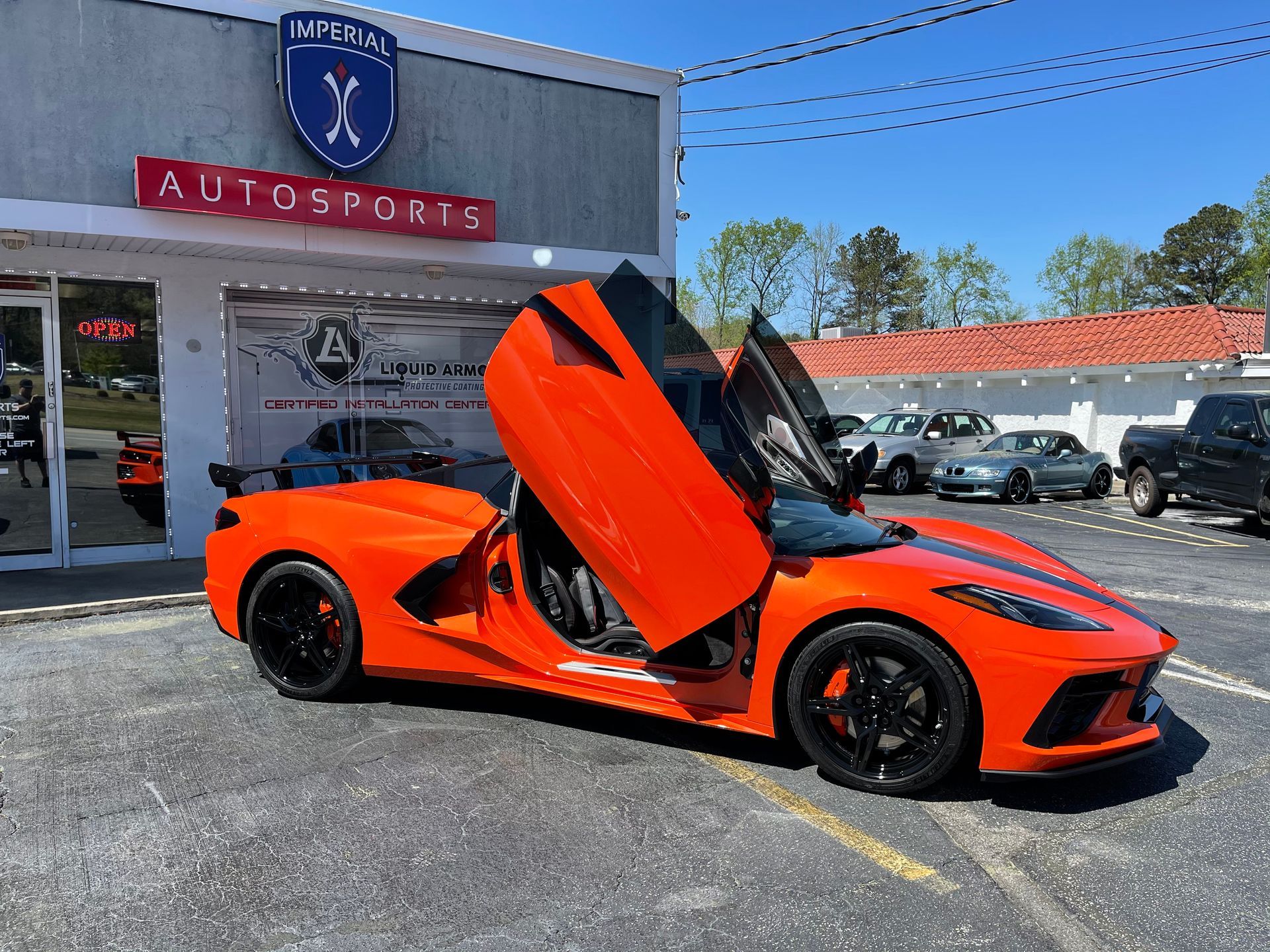 An orange sports car is parked in front of a car dealership.