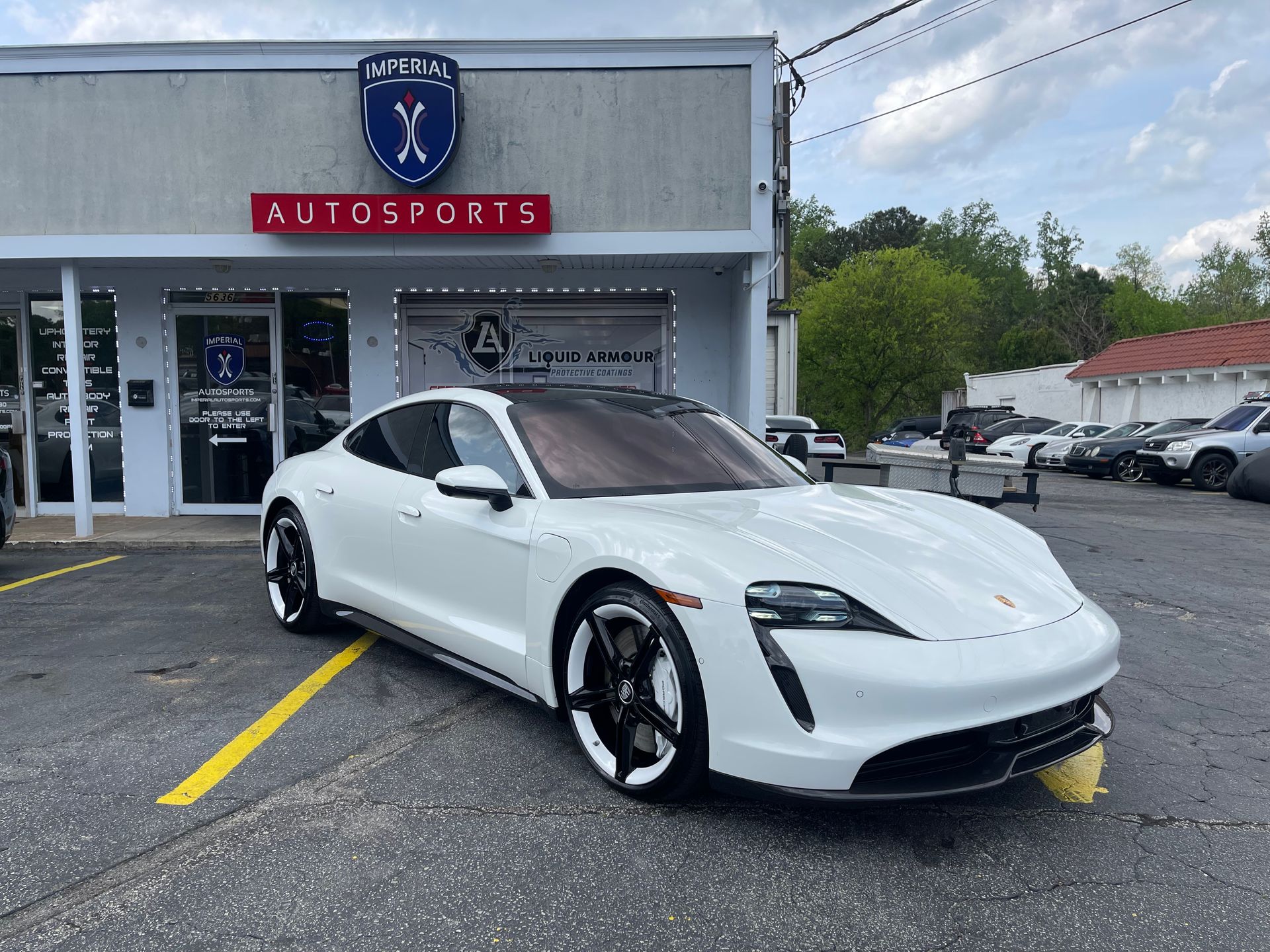 A white Porsche Taycan is parked in front of a car dealership