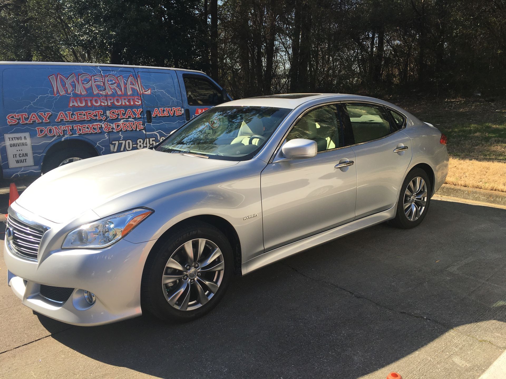 A silver car is parked on the side of the road next to a blue van