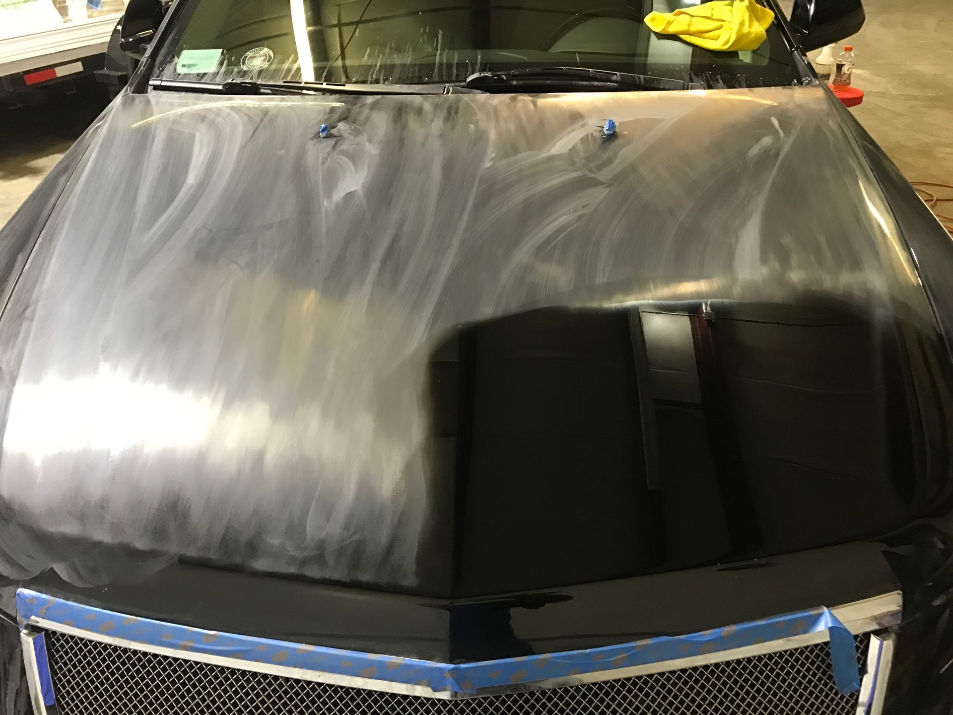 A black car with a blue tape around the hood is sitting in a garage