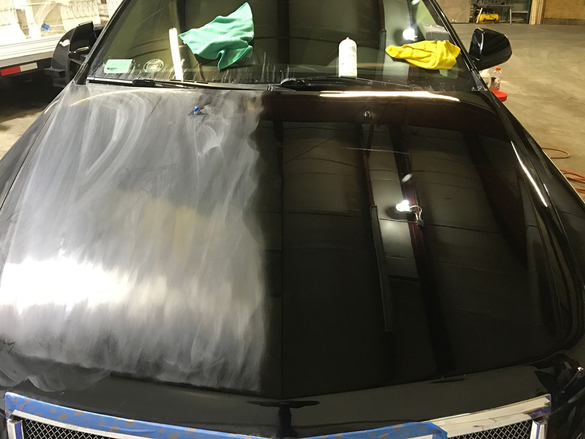 The hood of a black car is being cleaned in a garage