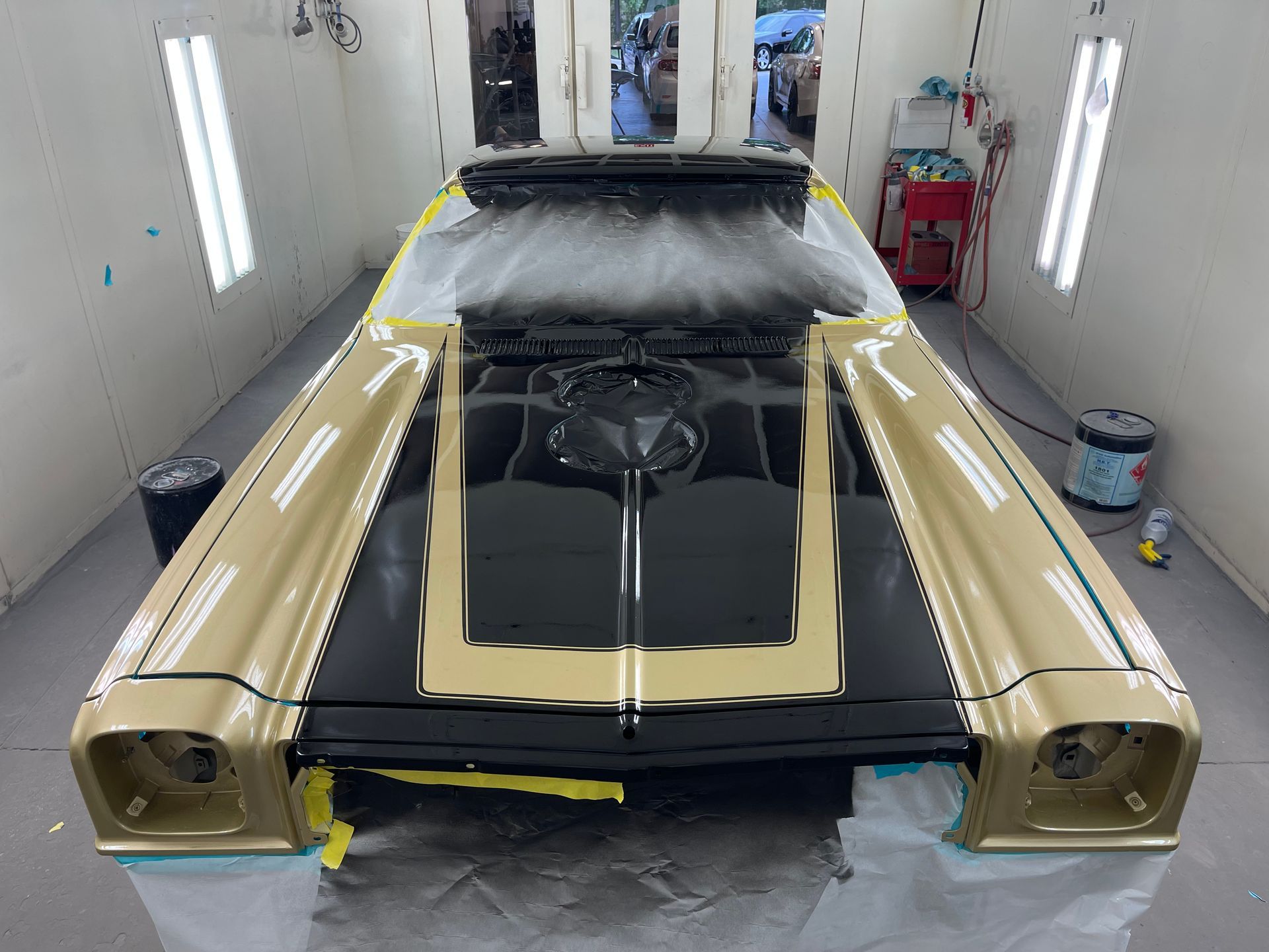 A black and gold car is being painted in a paint booth
