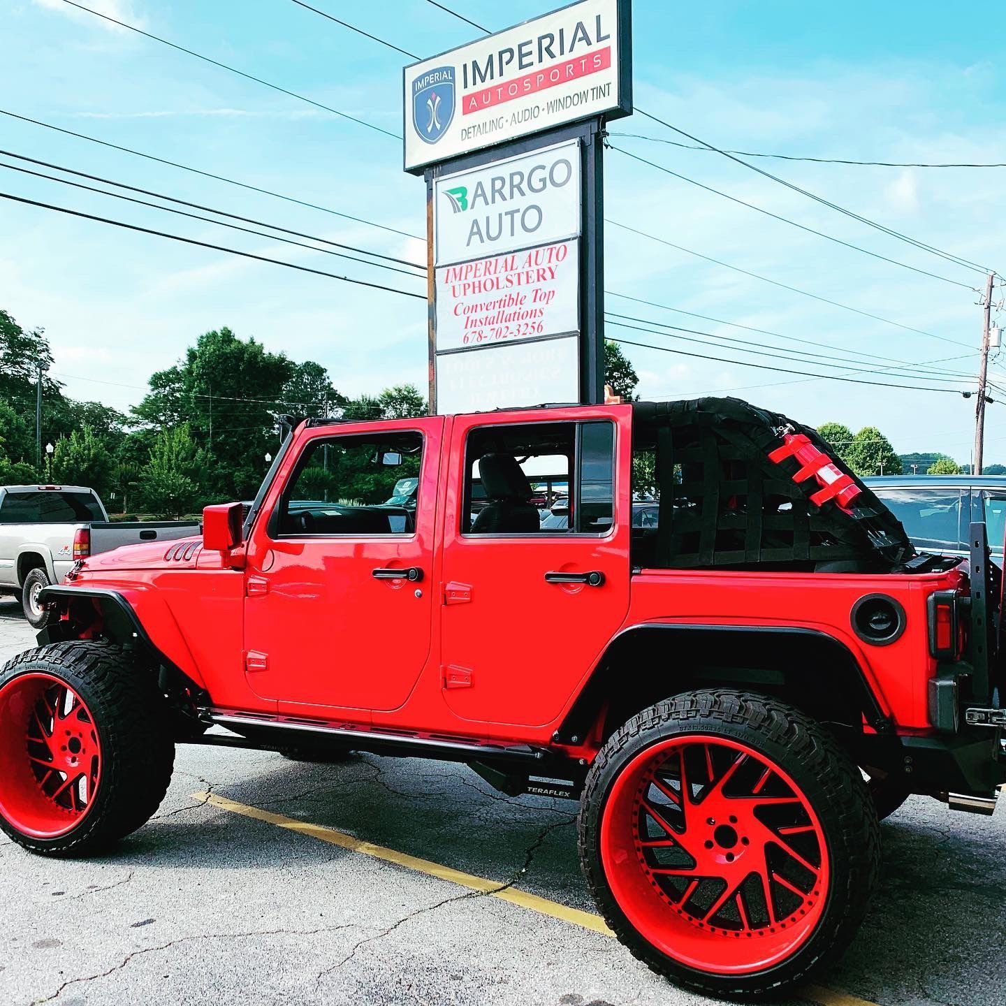 A red jeep is parked in front of a sign for imperial car dealership