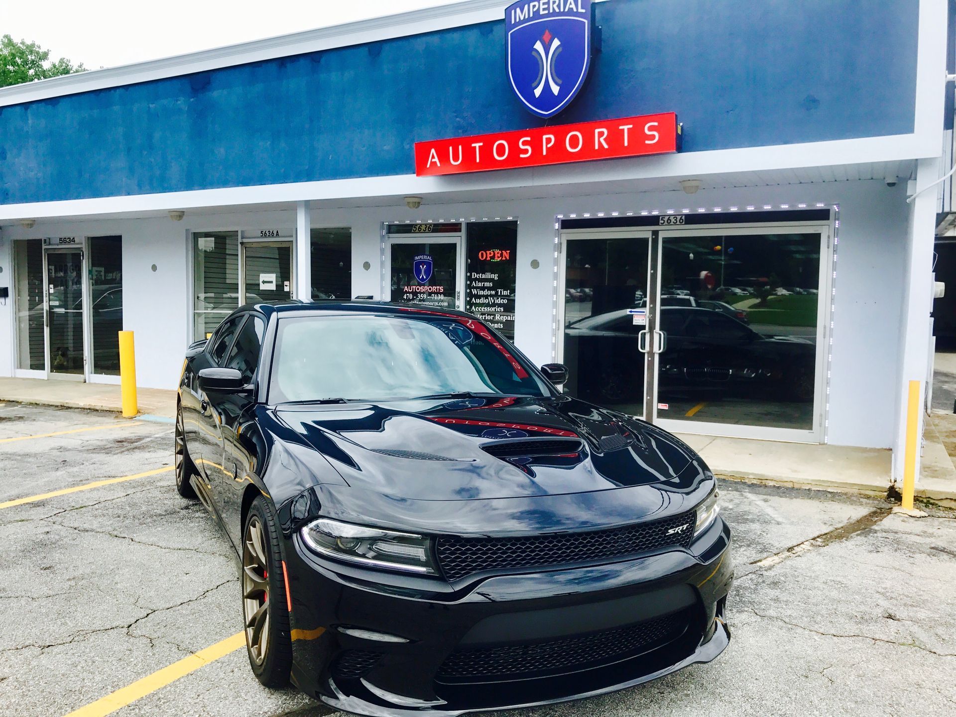 A black Dodge Charger is parked in front of a car dealership