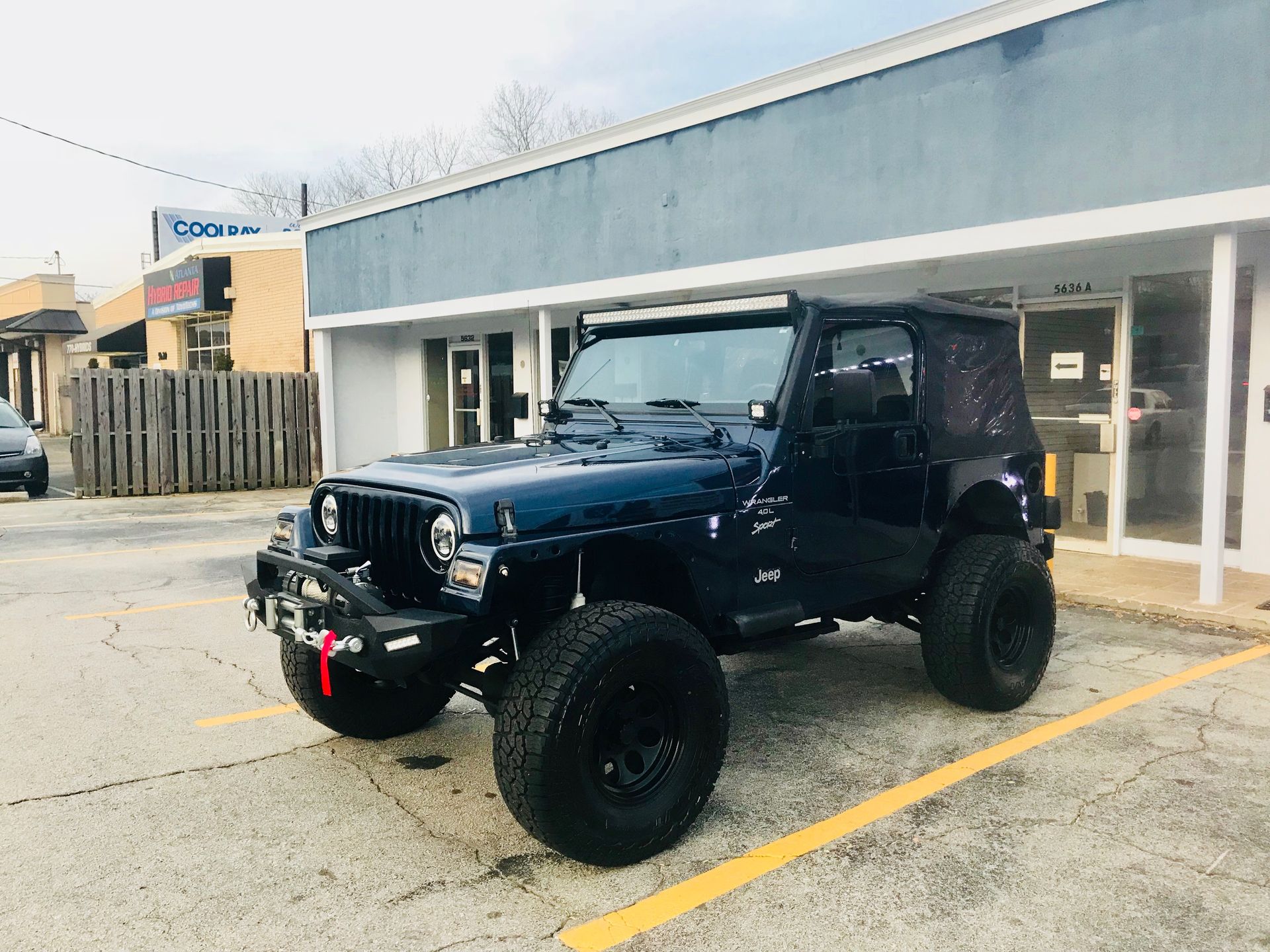 A blue Jeep is parked in a parking lot in front of a building