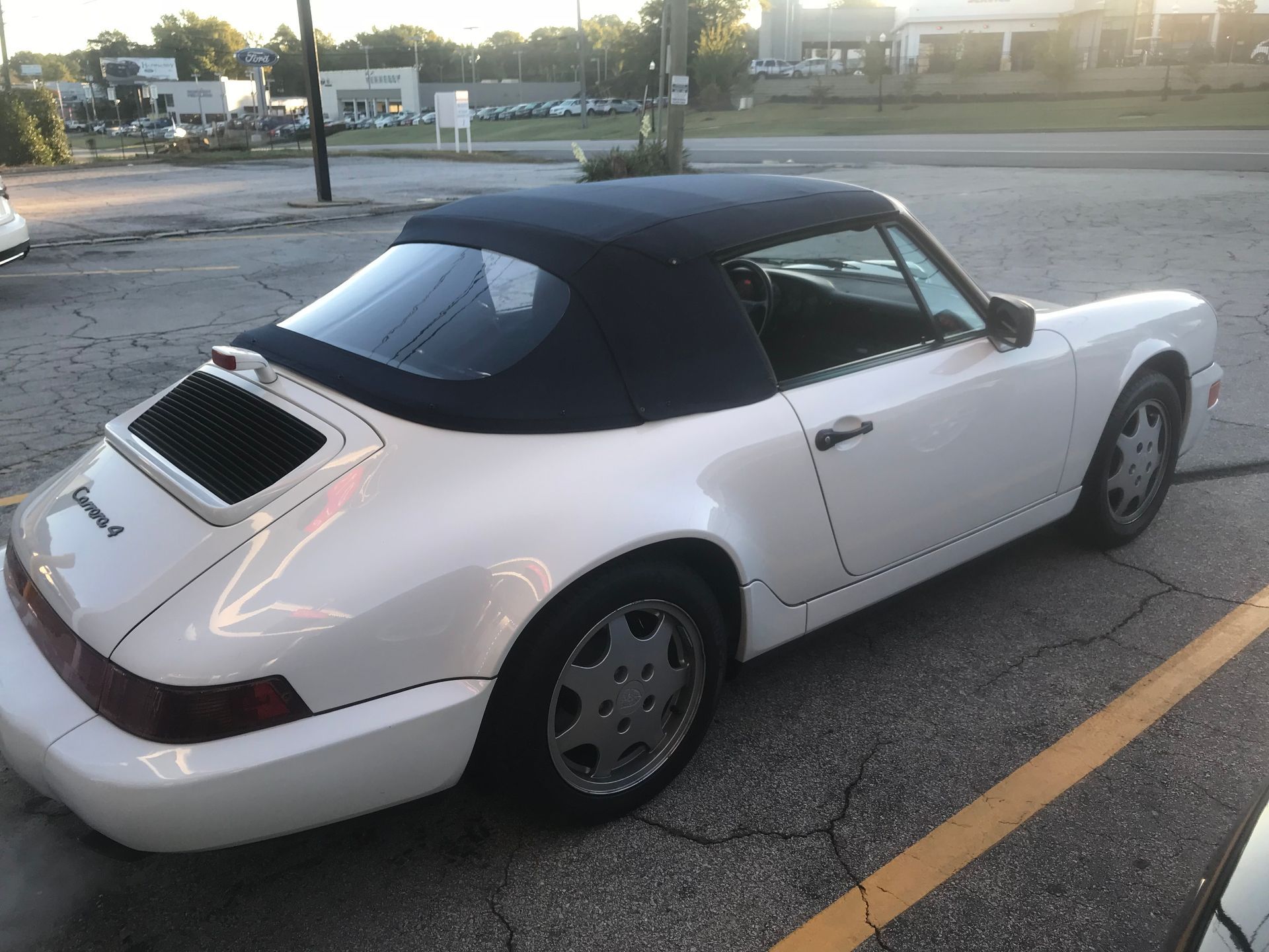 A white Porsche convertible is parked in a parking lot