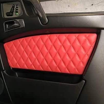 A close up of a red quilted leather door panel on a black car