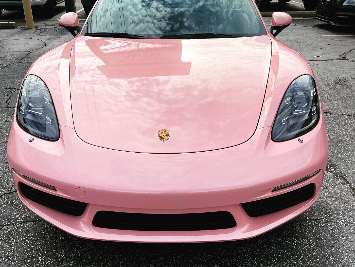 A pink Porsche is parked in a parking lot
