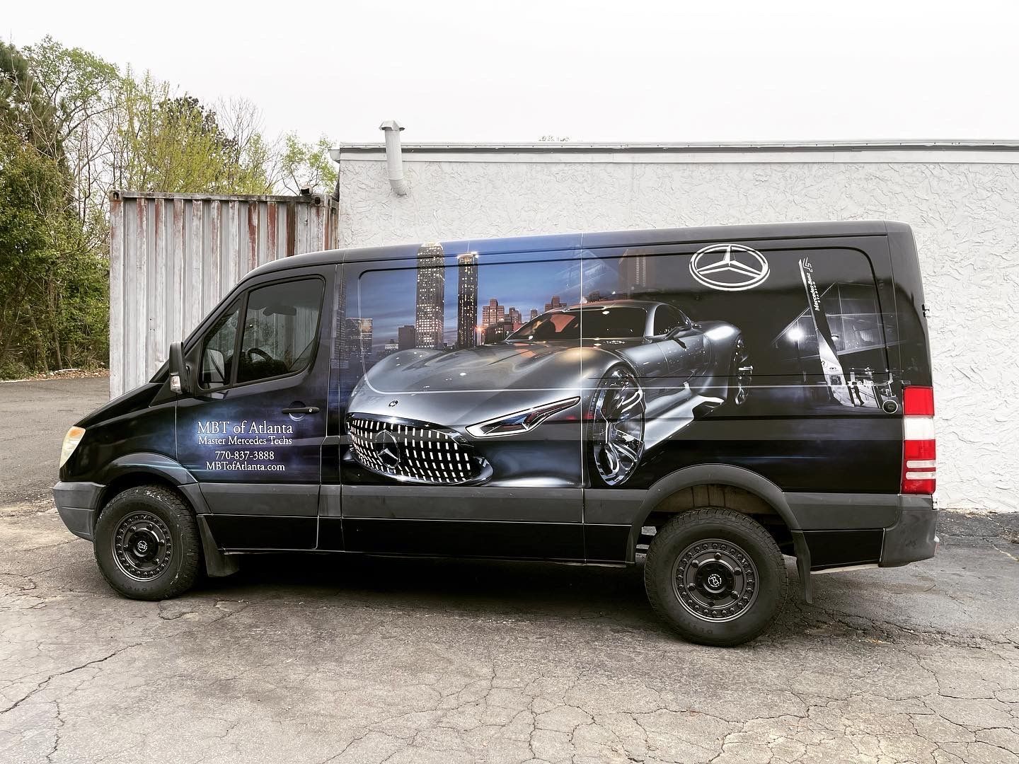 A black van with a picture of a car on the side is parked in front of a building