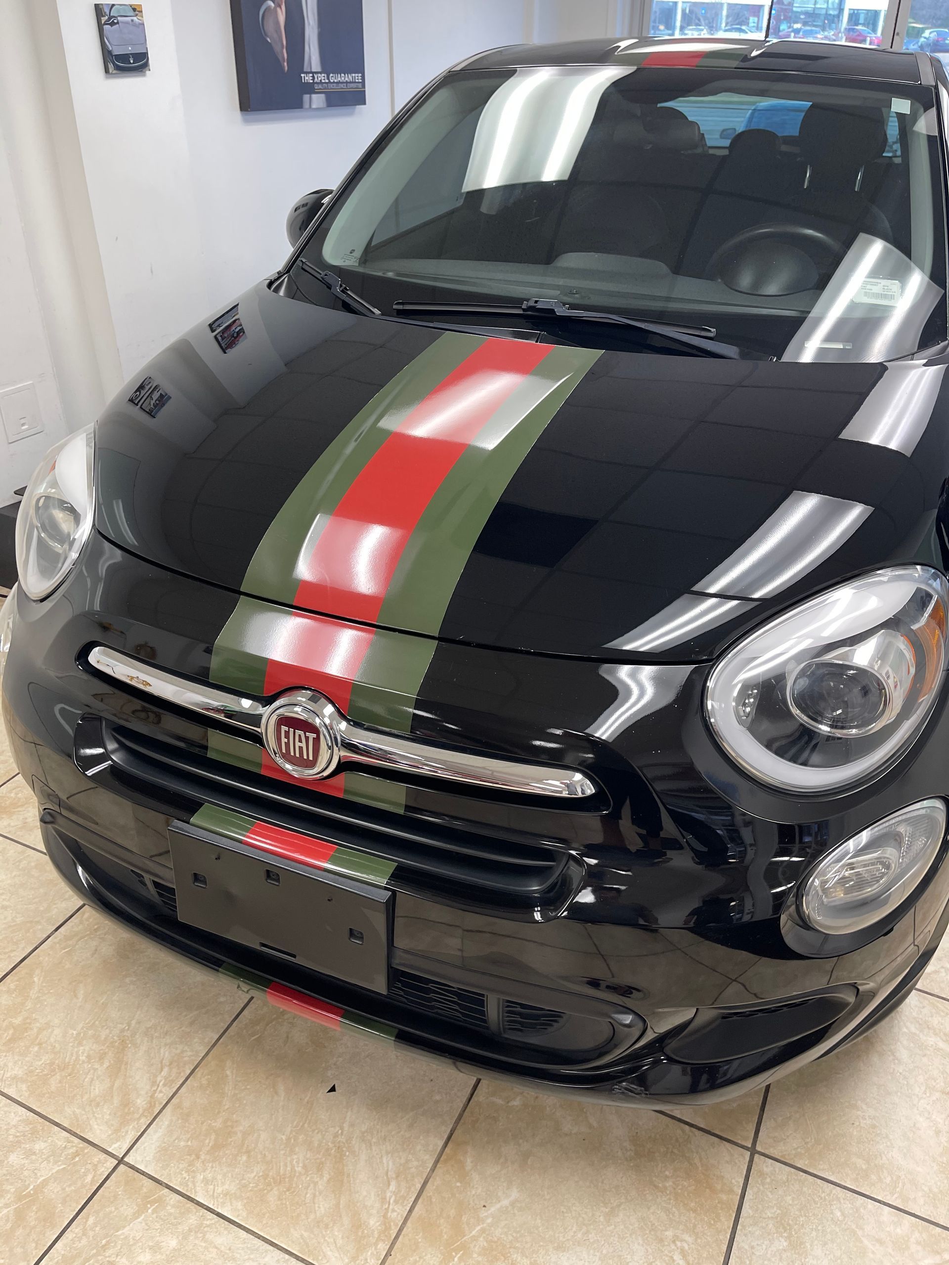 A black car with a red, green and white stripe on the hood is parked in a showroom