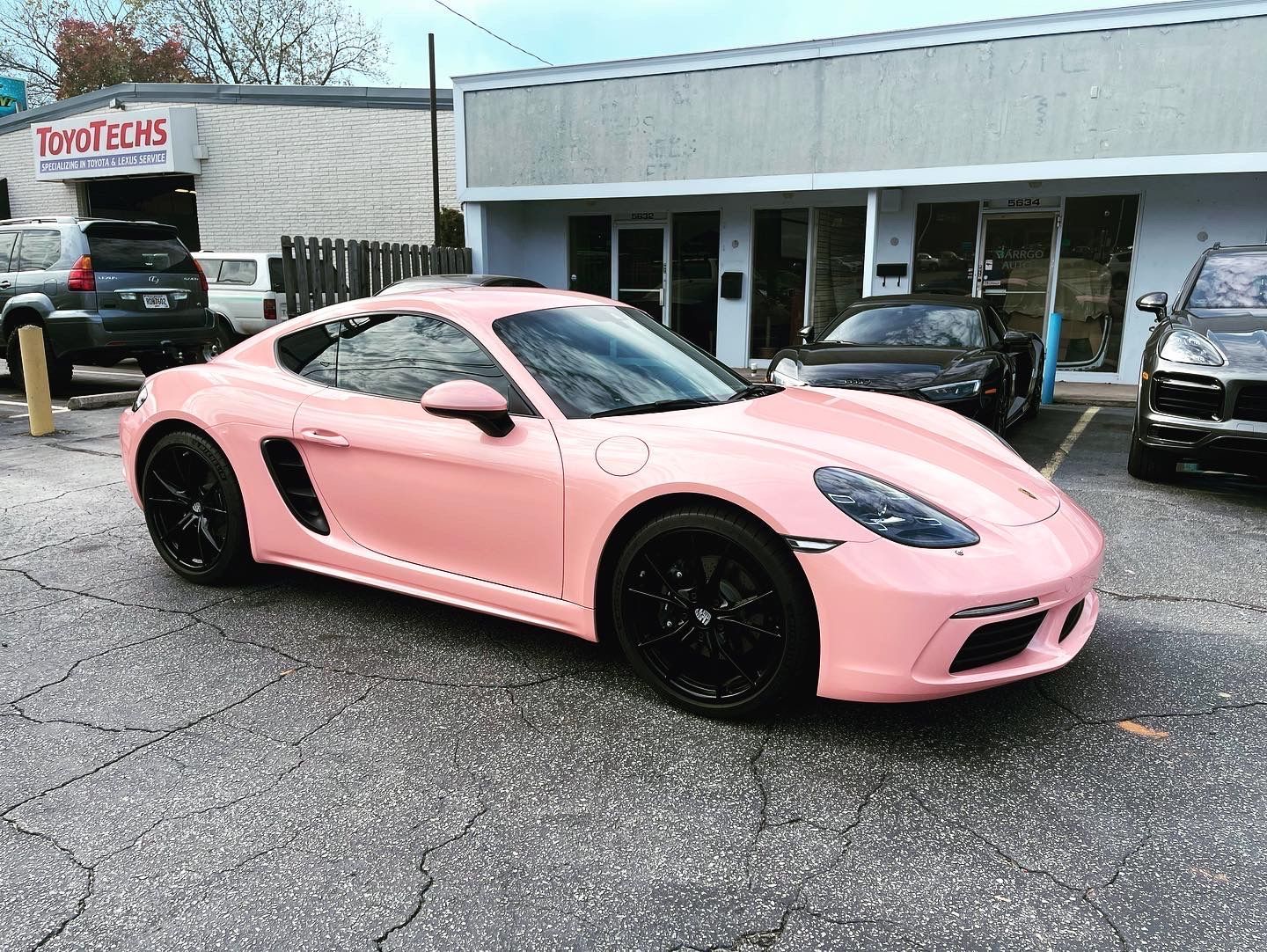 A pink Porsche Boxster is parked in front of a building
