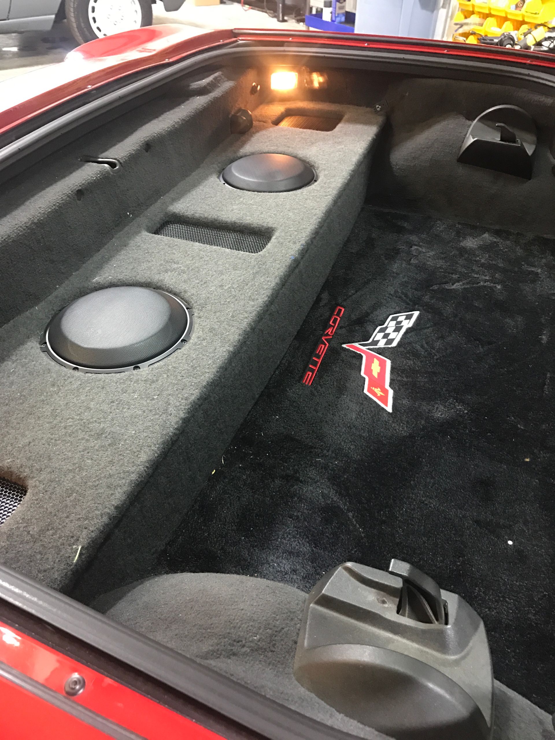 The trunk of a red corvette with speakers in it