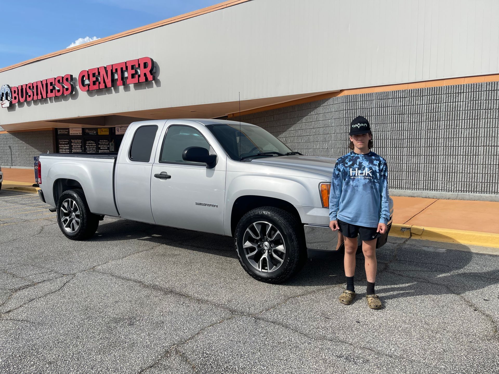 A boy is standing in front of a silver truck in a parking lot