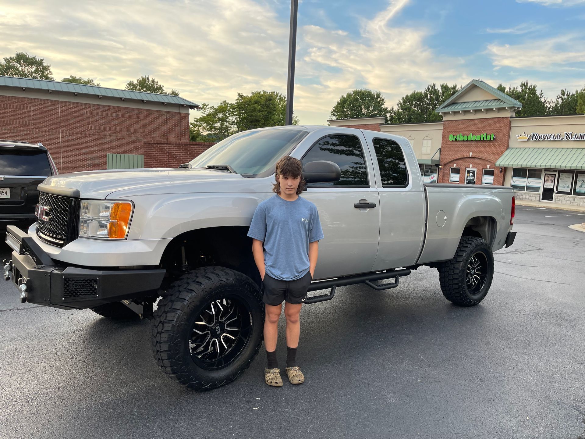 A young boy is standing in front of a silver truck