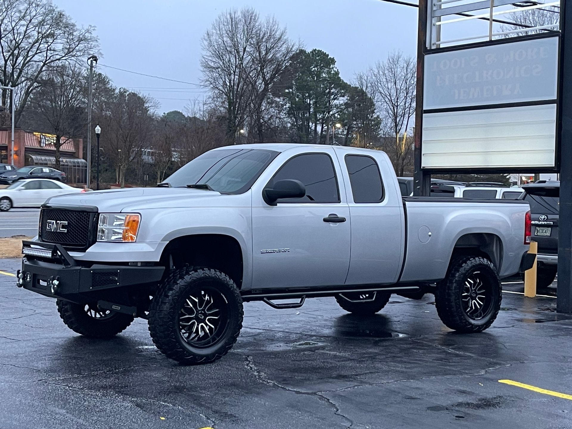 A silver pickup truck is parked in a parking lot in front of a building