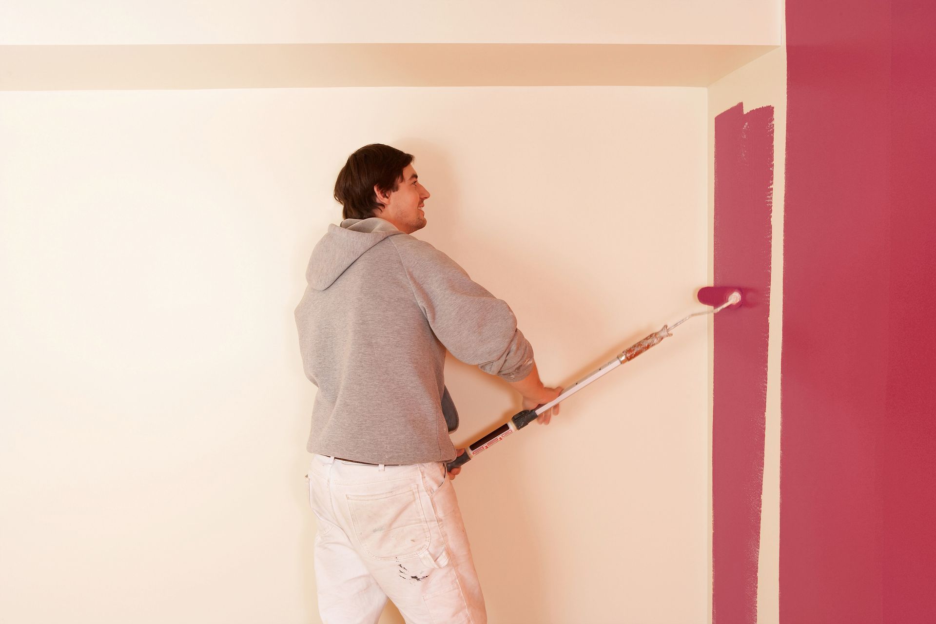 Person painting a wall with a roller. The wall is being painted pink.