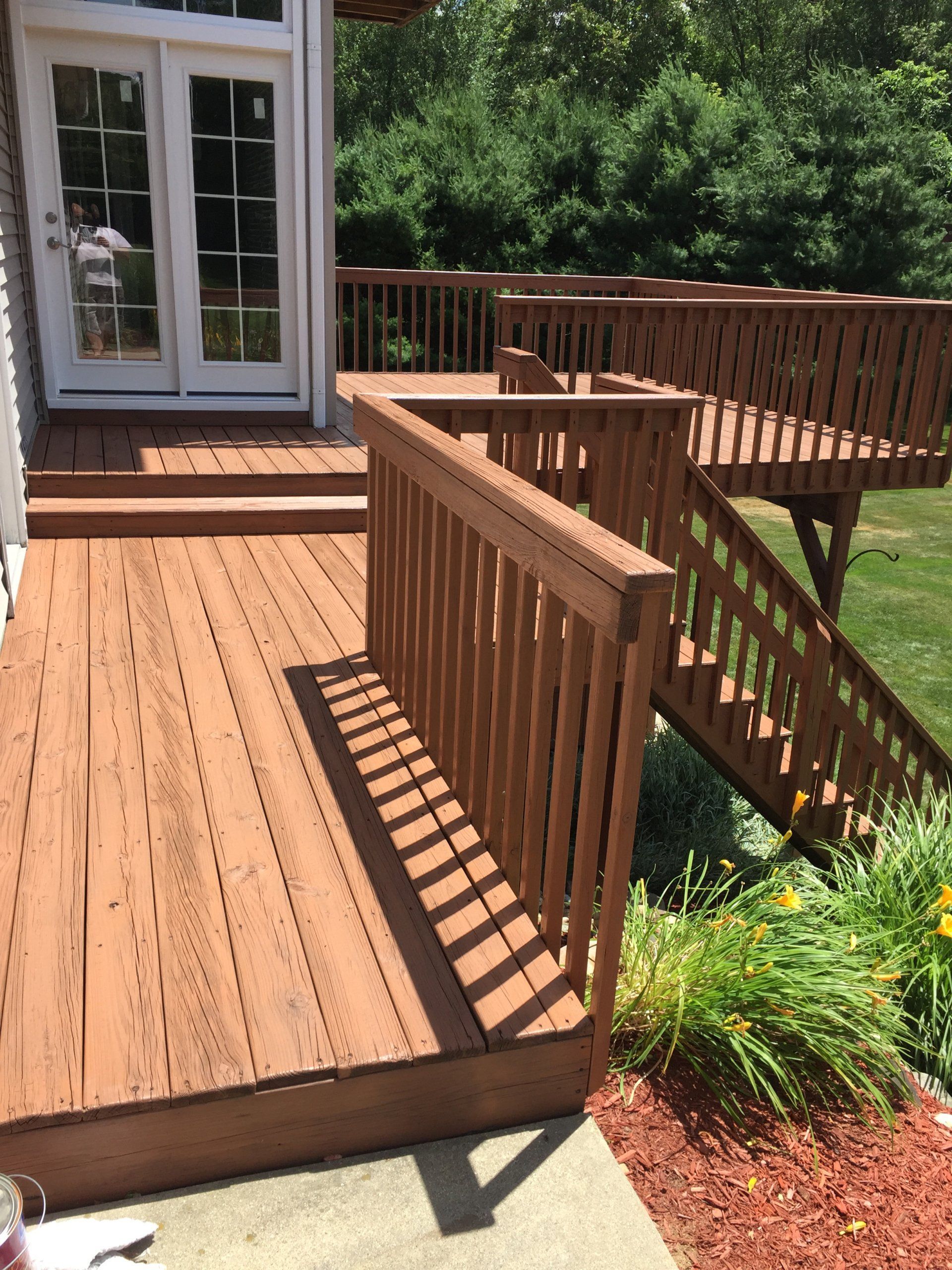 Wooden deck with brown stain, railings, and steps leading to a yard with grass and trees.