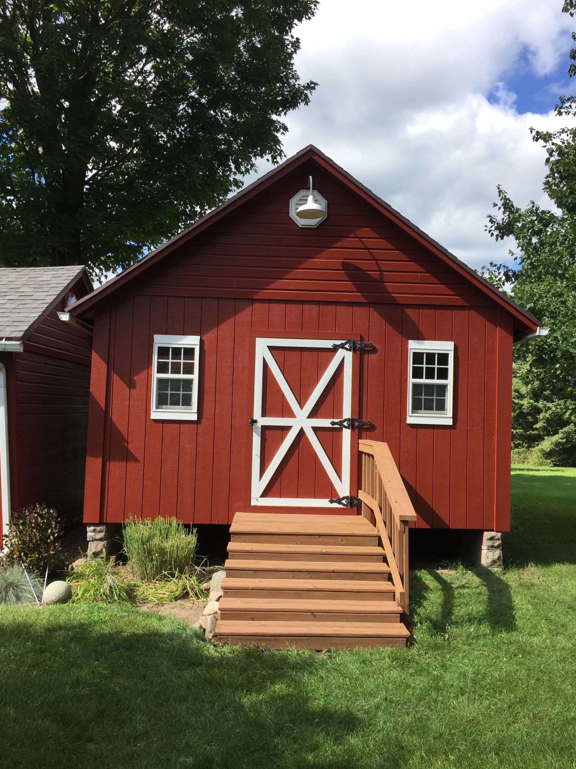 Red barn with white trim, wooden door, and steps, in a grassy setting.