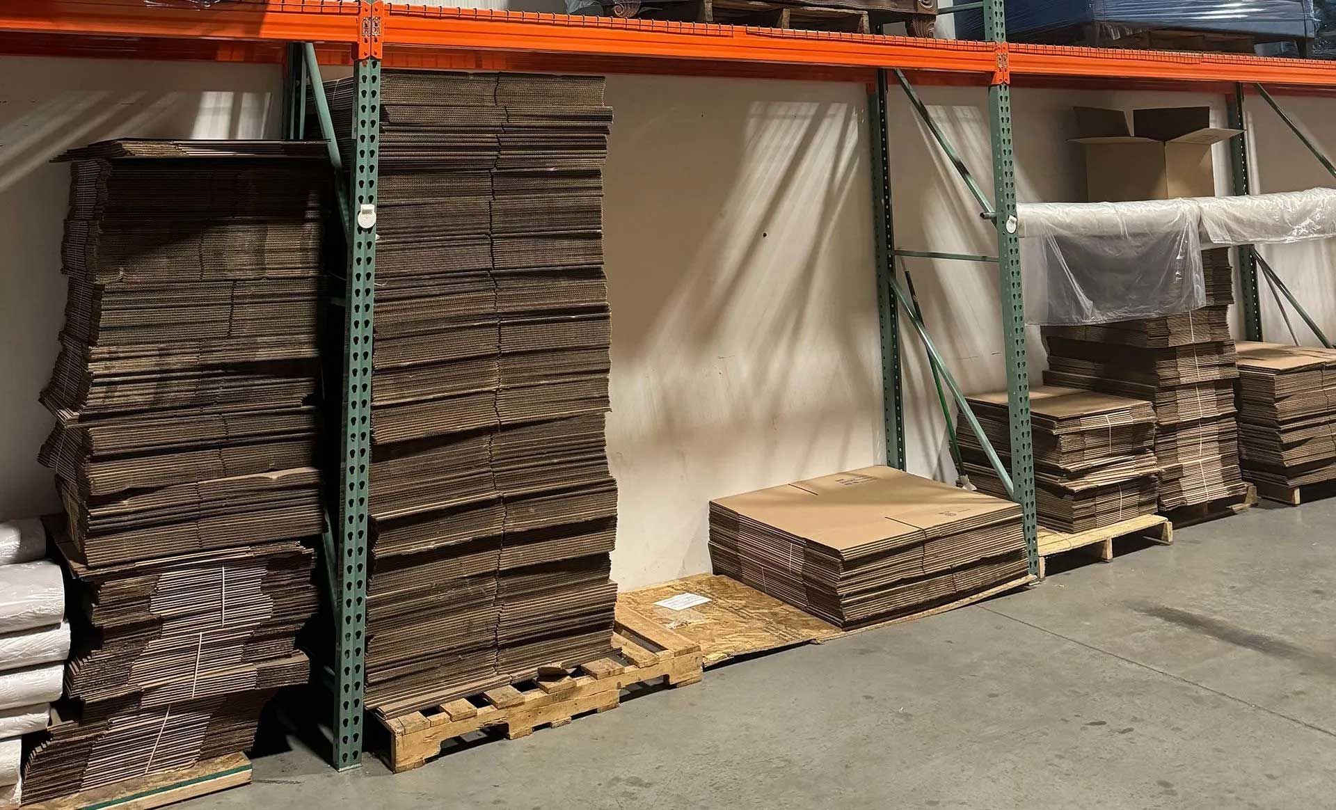 Stacks of cardboard sheets and boxes stored on pallets in a warehouse.