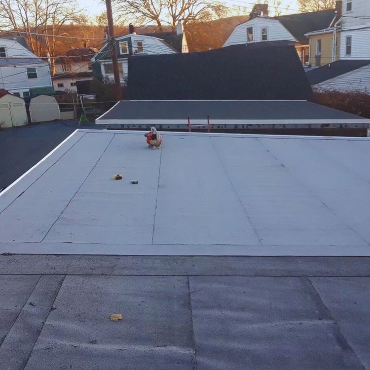 Flat rooftop with a small person near the center, surrounded by neighboring houses at sunset.