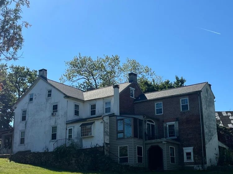 Old white house with a brick section under a blue sky and trees