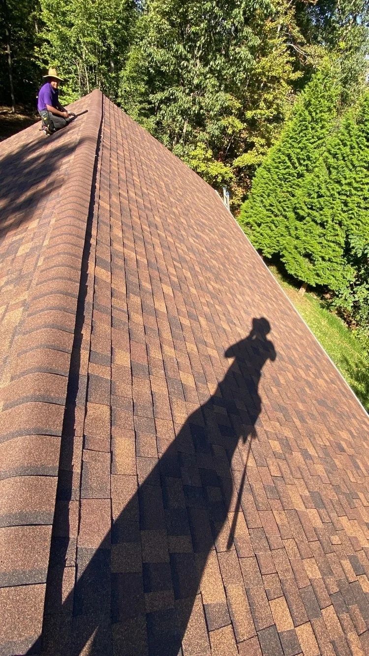 Roof viewed from above, with a worker on the left and a long shadow cast across brown shingles.