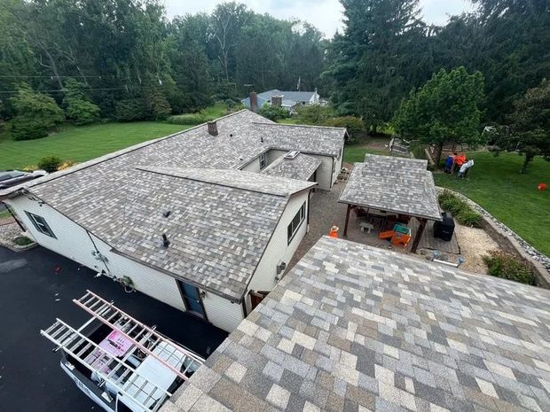 Aerial view of a building with a gray shingled roof, surrounded by trees and a lawn.