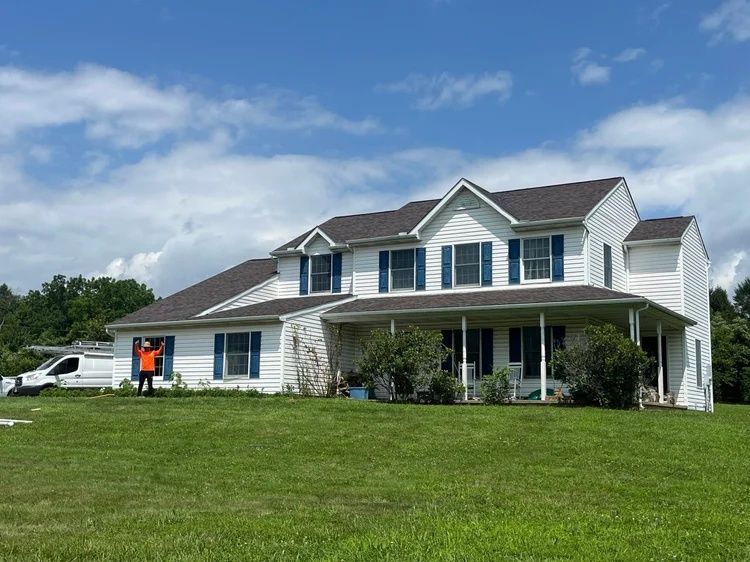 Two-story white house with a front porch and green lawn under a partly cloudy blue sky