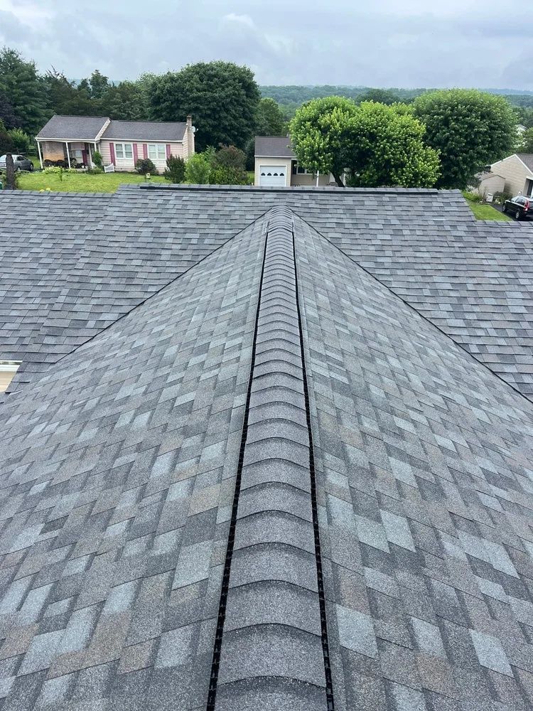 Gray shingled roof with a central ridge, viewed toward trees and houses in the distance