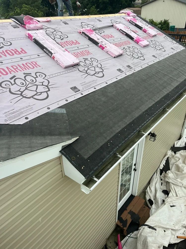 Roof under repair with pink insulation boards and housewrap on a beige home.