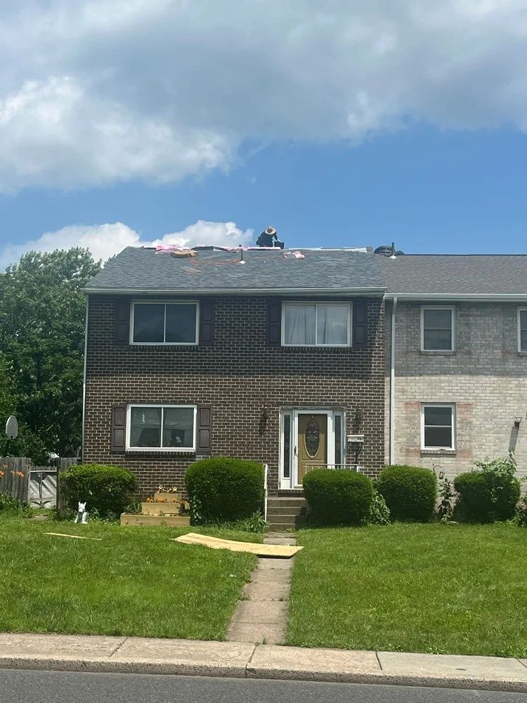 Two-story brick townhouse with a front lawn, walkway, and bushes under a cloudy sky.