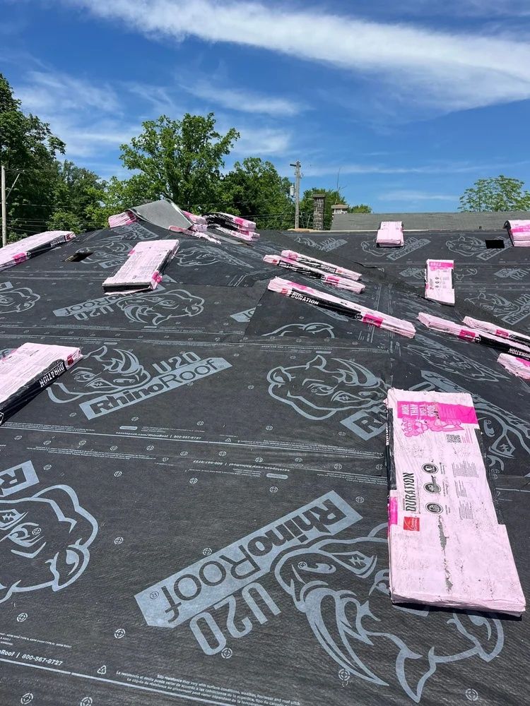 Roof under construction with black underlayment, pink insulation boards, and a blue sky overhead