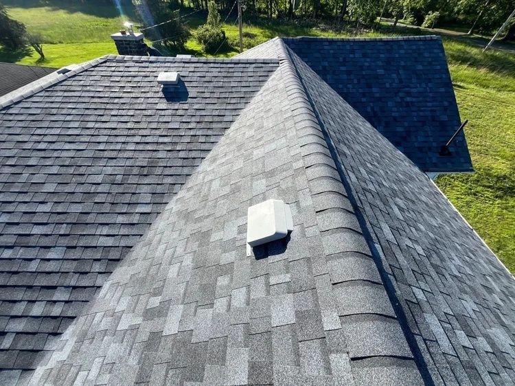 Roof with dark gray shingles and two white vents, viewed from above on a sunny day