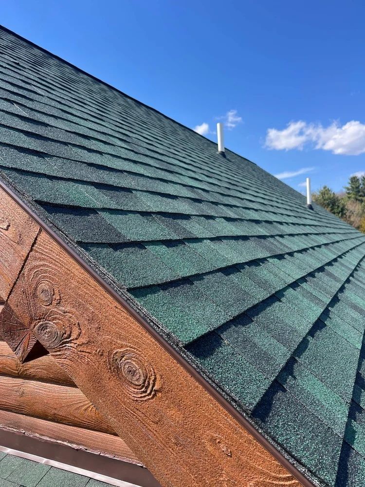 Close-up of a green shingled roof with a decorative copper edge against a blue sky